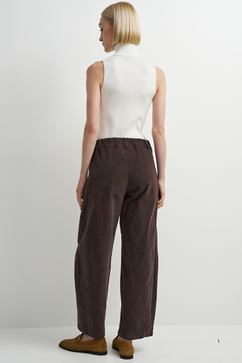 A woman shown from the back wearing a white sleeveless mock-neck top and dark brown wide-leg trousers, paired with brown suede shoes, against a plain white studio background.