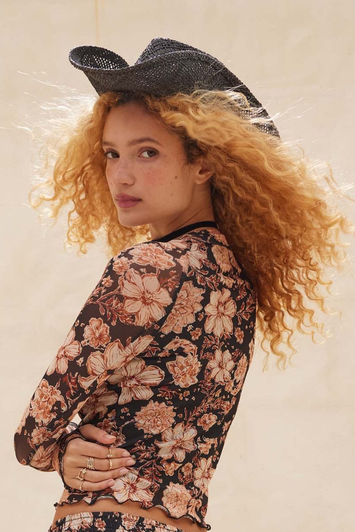 Woman wearing a floral outfit and cowboy hat against a neutral background