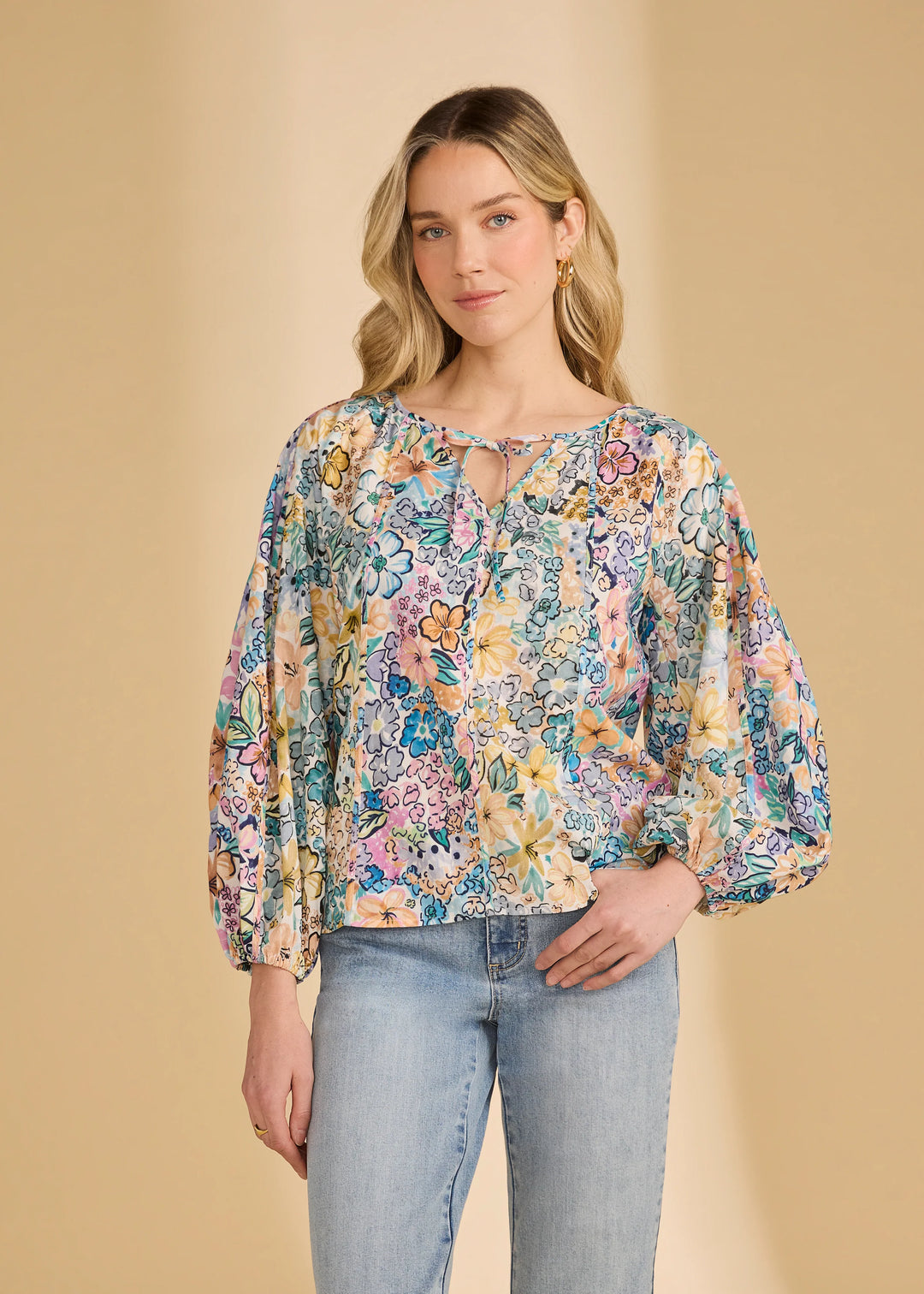 Woman wearing a floral blouse and jeans against a beige background