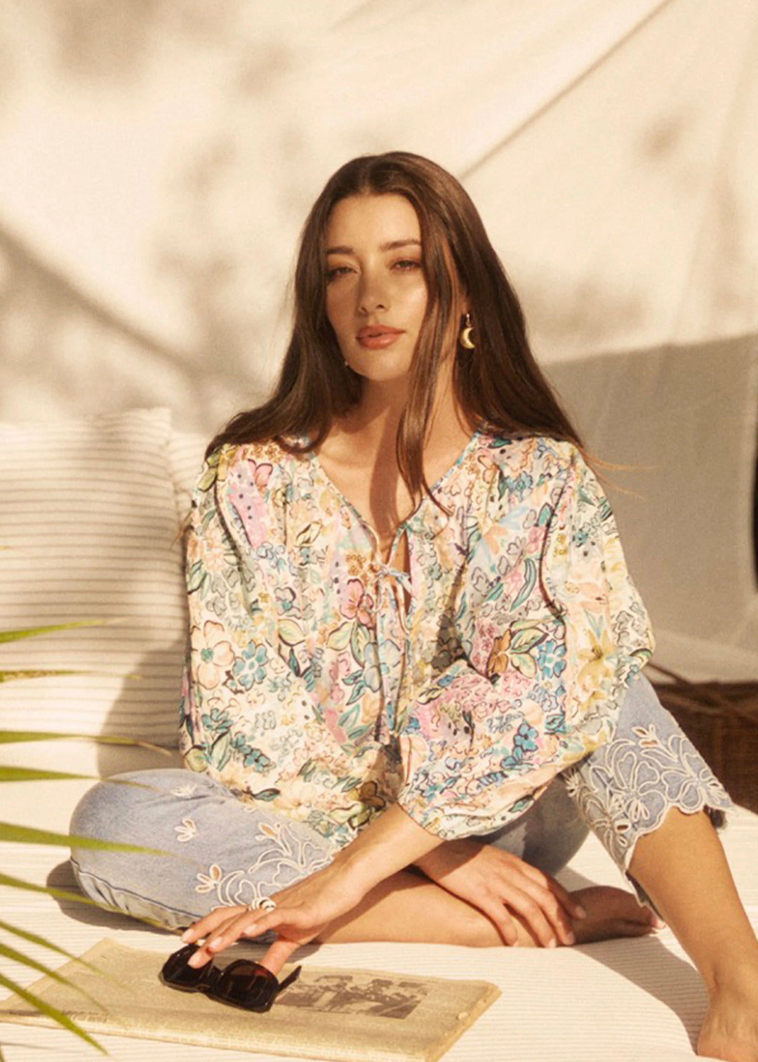 Woman sitting outdoors wearing a floral blouse and light pants.