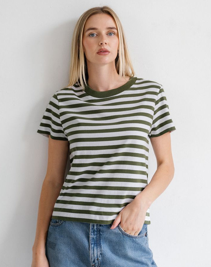 A woman wearing a short-sleeve crewneck t-shirt with horizontal olive green and off-white stripes, paired with blue jeans, standing against a plain white wall.
