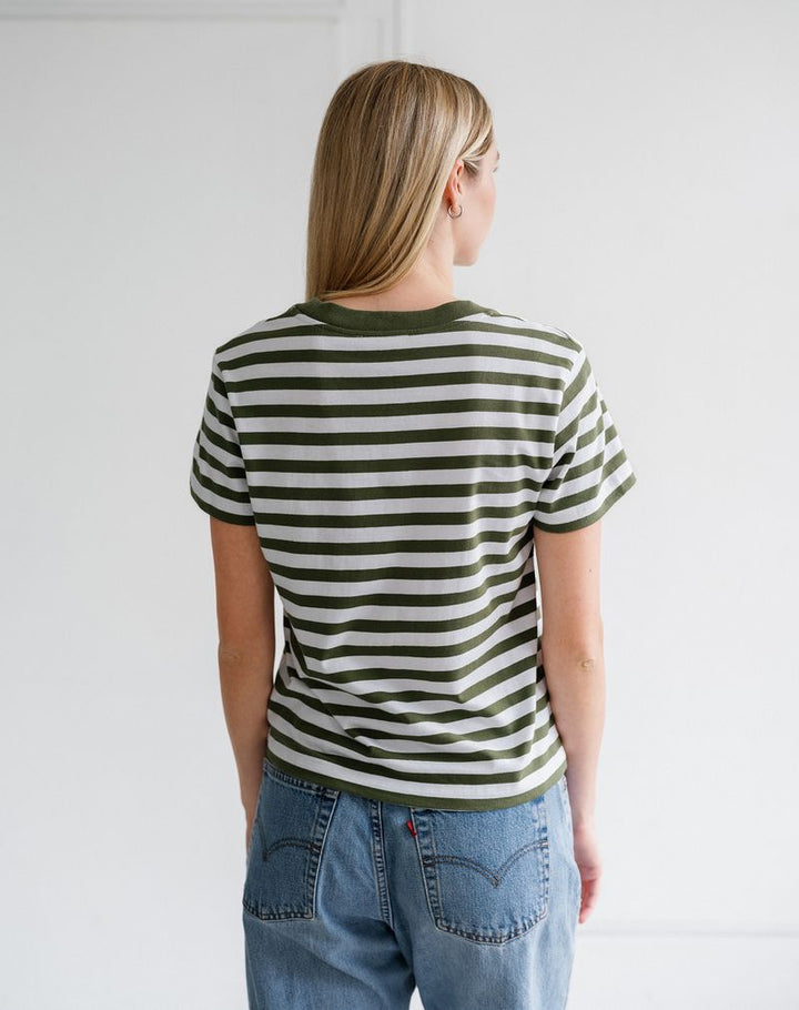 A woman viewed from behind wearing a short-sleeve crewneck t-shirt with horizontal olive green and off-white stripes, paired with blue jeans.