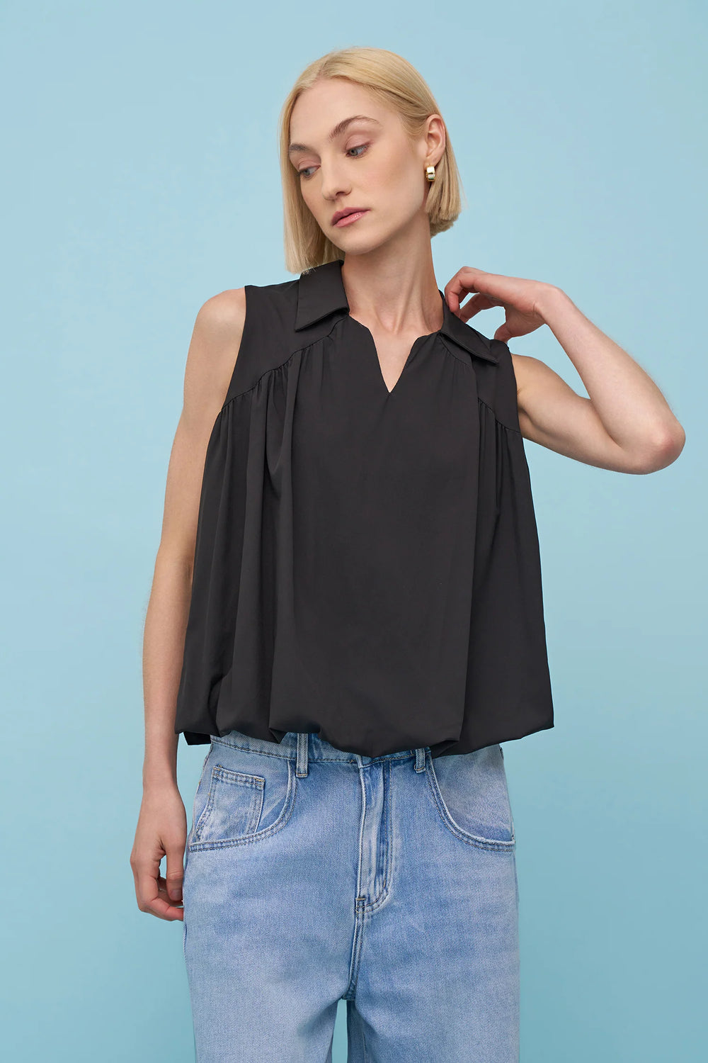 Woman wearing a black sleeveless top and blue jeans against a light blue background