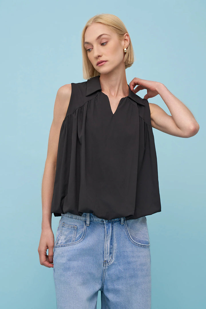 Woman wearing a black sleeveless top and blue jeans against a light blue background