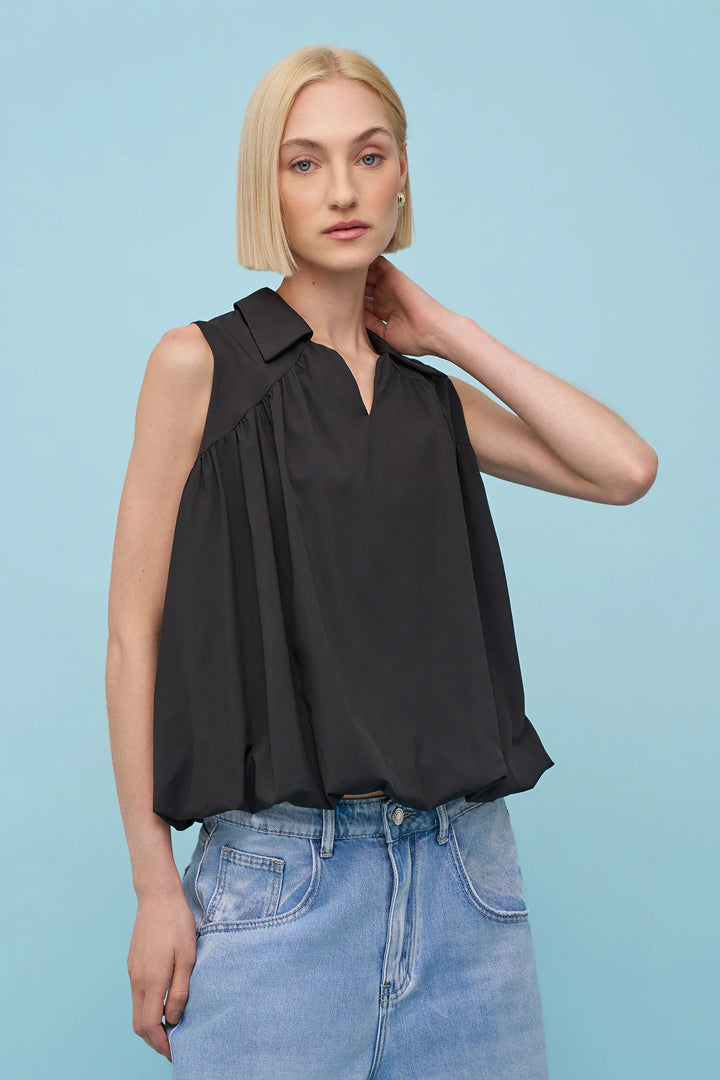 Woman wearing a black sleeveless top and blue jeans against a light blue background