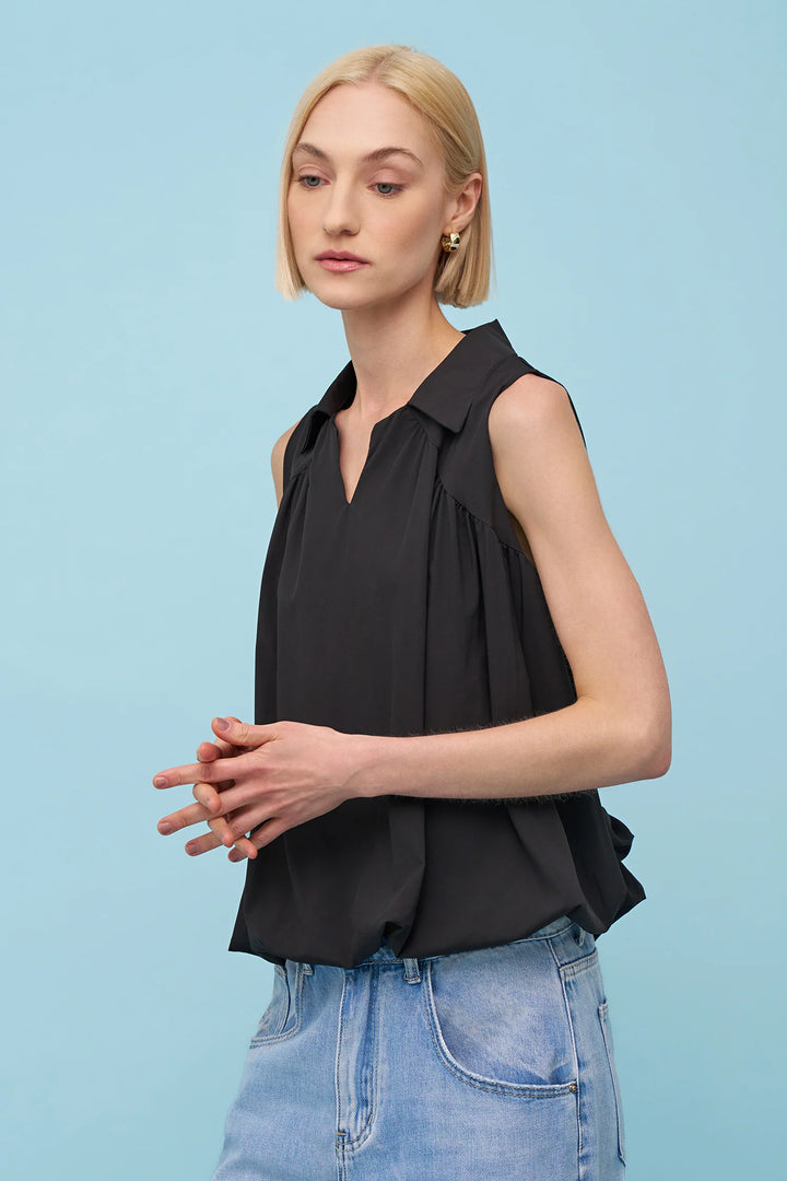 Woman wearing a black sleeveless top and blue jeans against a light blue background