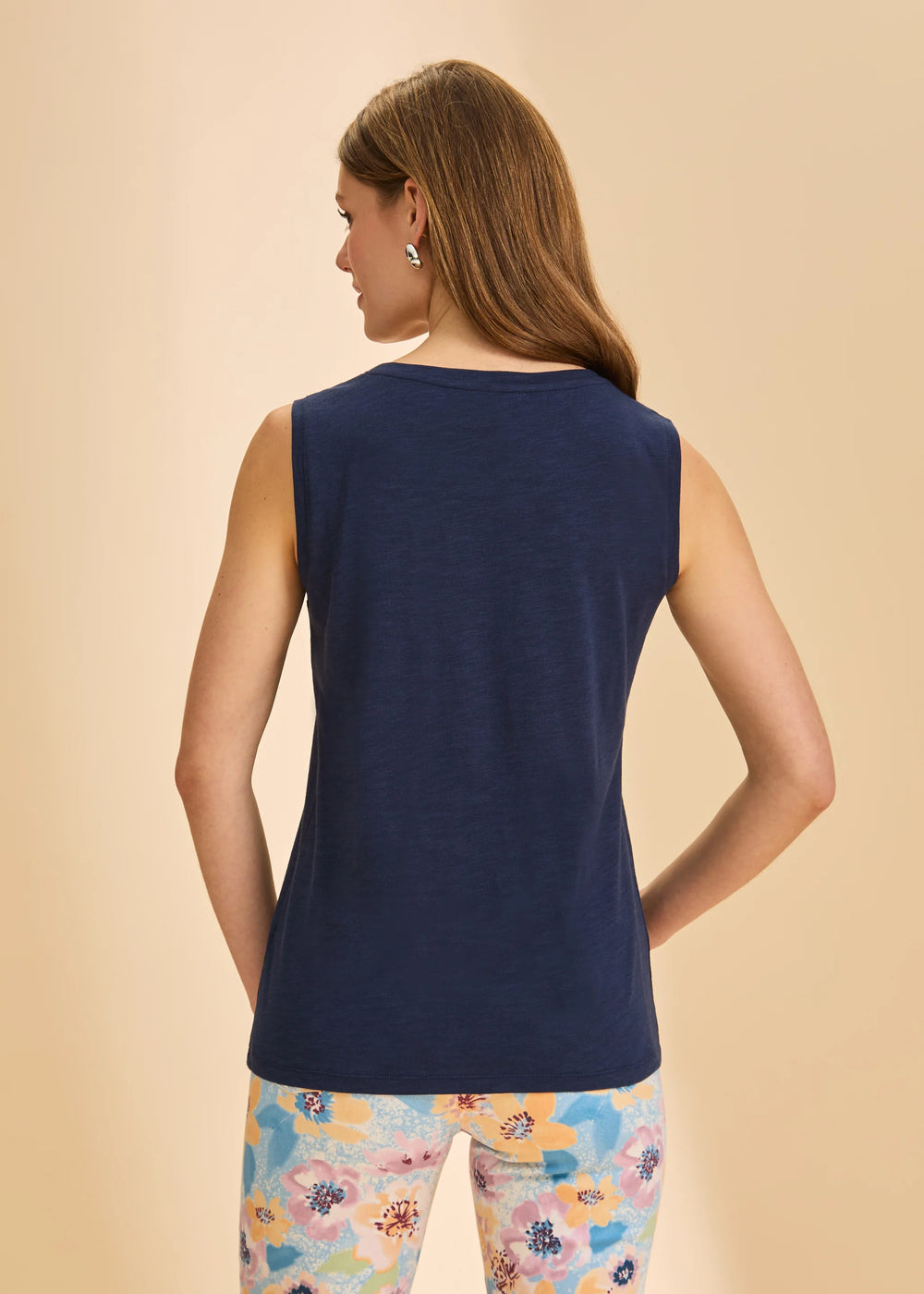 Woman wearing a navy sleeveless top and colorful floral pants on a beige background