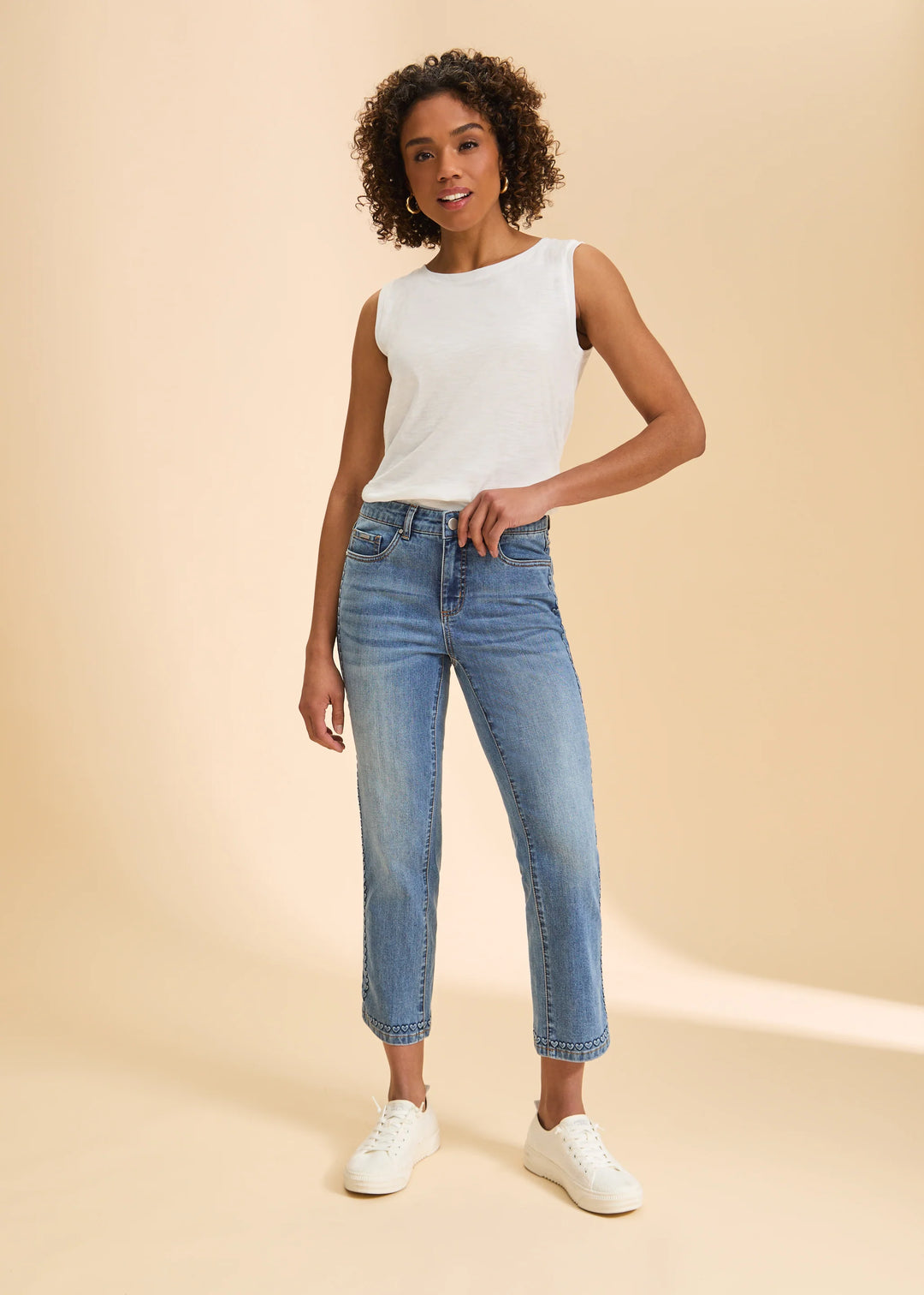 Woman wearing a white sleeveless top and blue jeans on a beige background