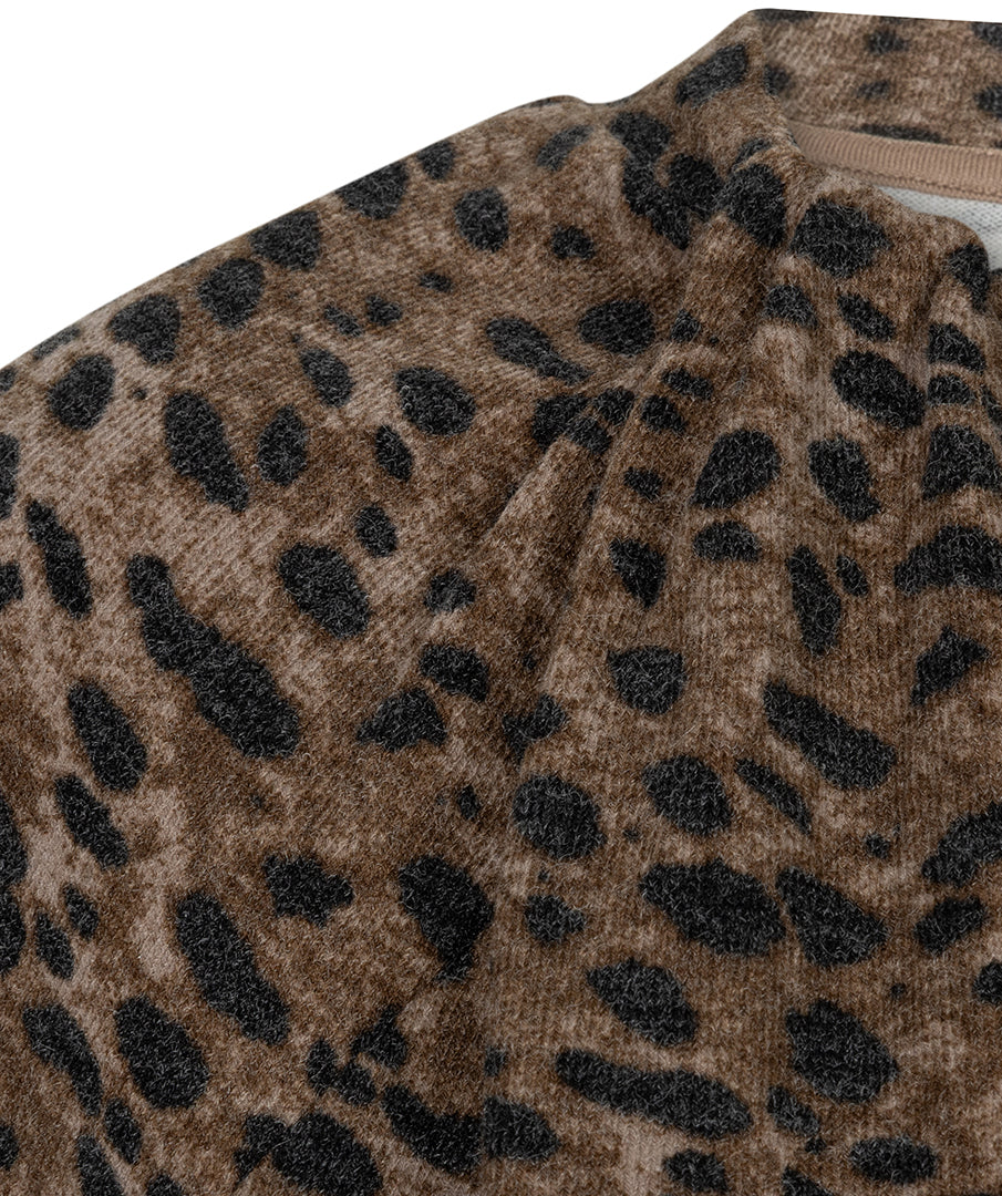 Close-up of a leopard print fabric with a soft, plush texture, featuring a brown base with black spots and a beige inner collar lining.