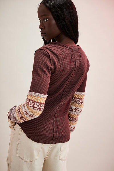 Person wearing a maroon sweater with patterned sleeves against a plain background