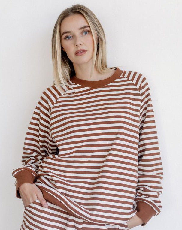 A woman modeling a matching brown and white striped lounge set, featuring a long-sleeve top and shorts, against a plain white background.