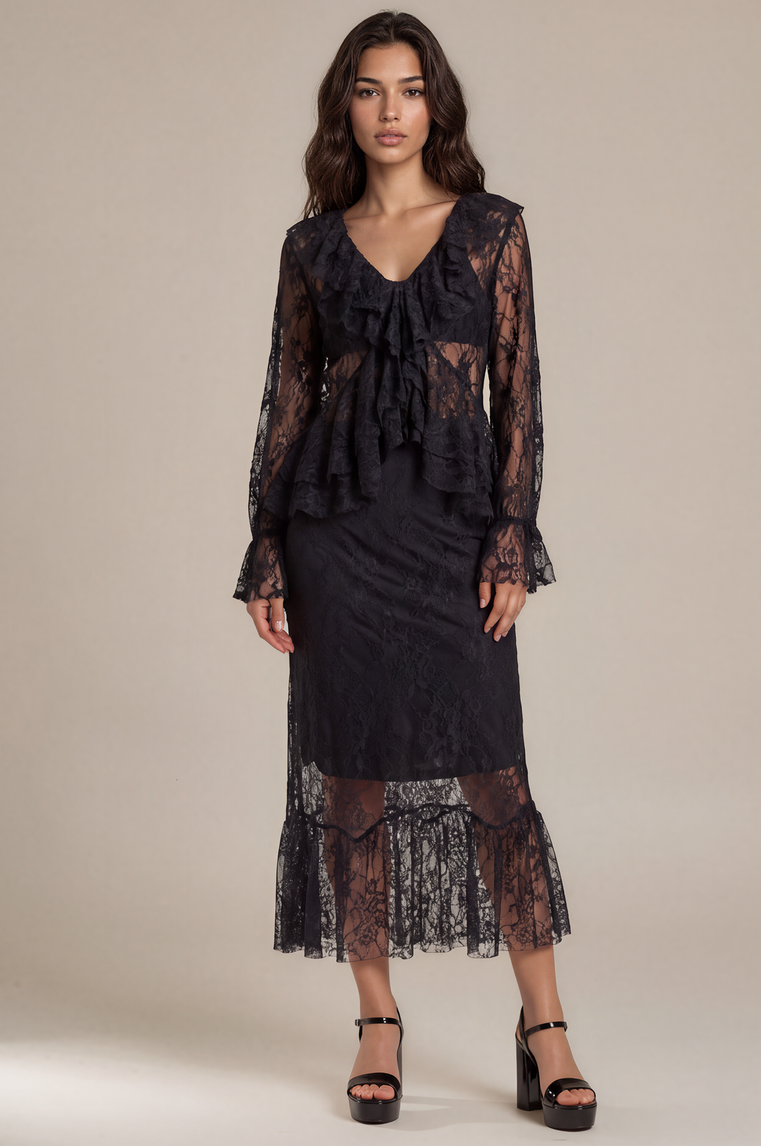 A model wears a black lace long-sleeve midi dress with a ruffled V-neckline and tiered hem, paired with black platform sandals, against a solid beige studio background.