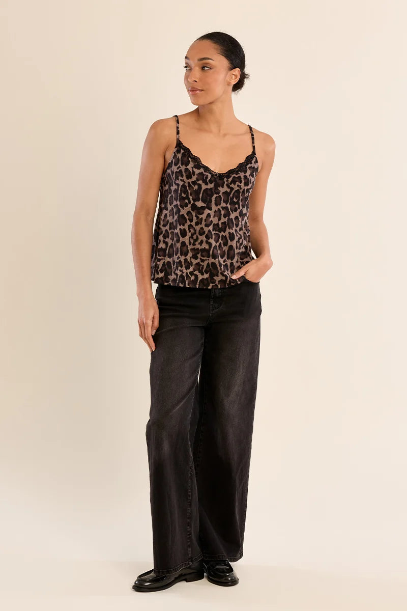 A woman modeling a leopard print camisole top with black wide-leg jeans and black shoes, standing against a plain beige studio background.