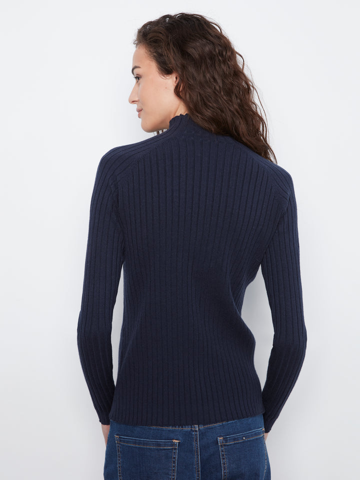 A woman with long dark curly hair is shown from the back wearing a navy blue ribbed knit mock neck sweater and blue jeans against a plain white background.