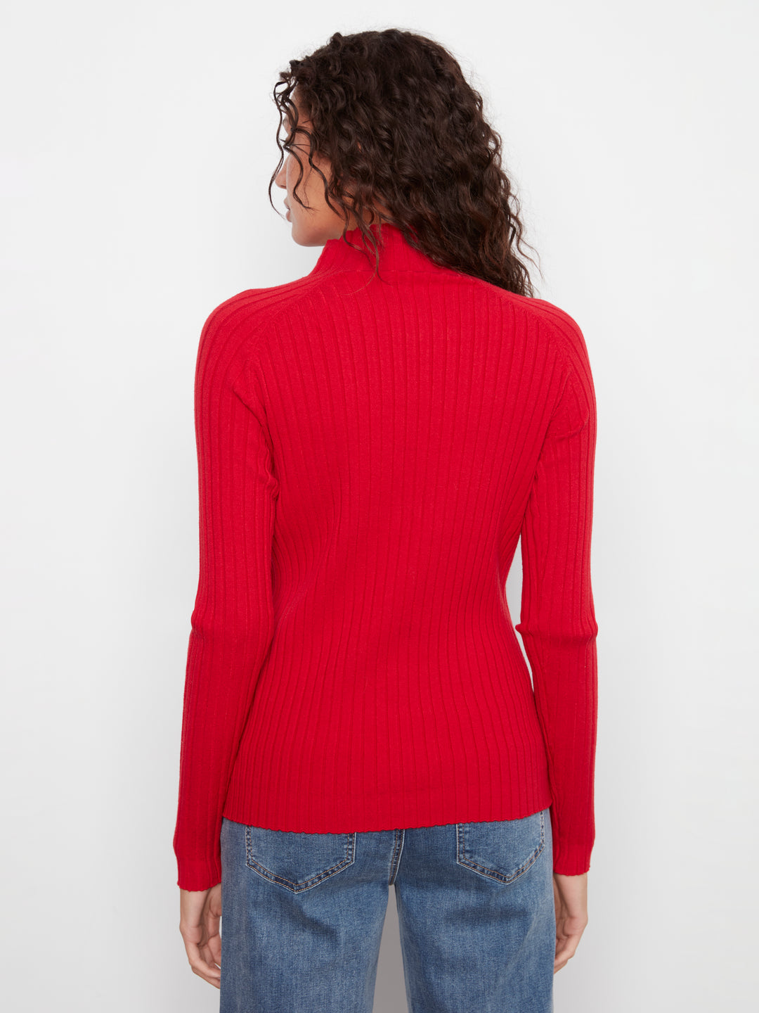 Person wearing a red ribbed turtleneck sweater and blue jeans on a white background