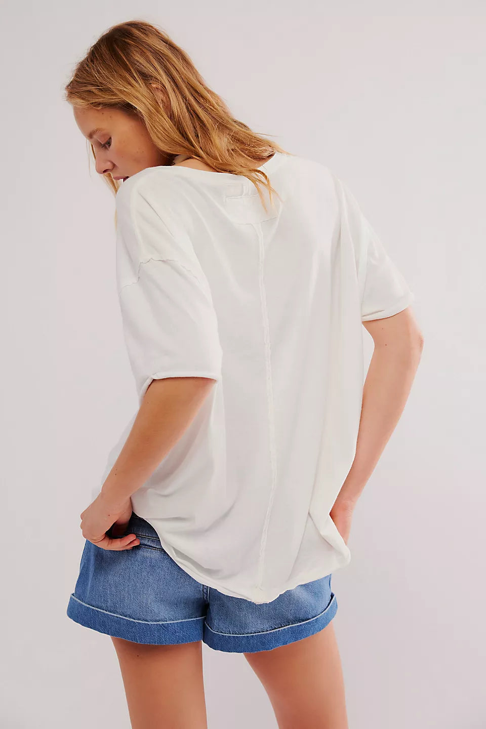 Person wearing a white oversized t-shirt and blue shorts on a plain background