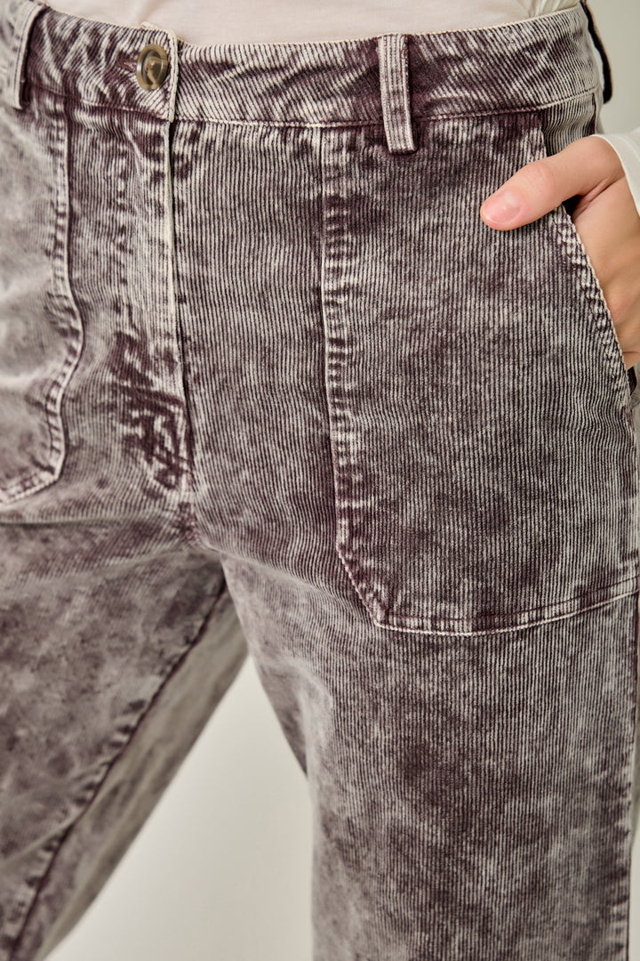 Close-up of a person wearing washed charcoal corduroy trousers, showing the front pocket, belt loops, waistband, and a hand in the pocket.