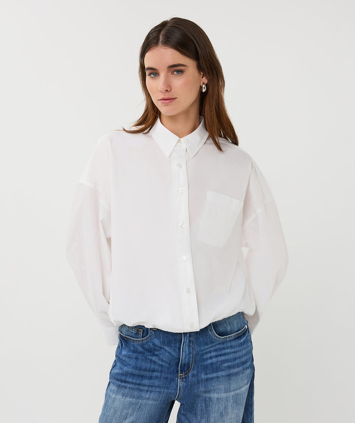 Woman wearing a white shirt and blue jeans against a plain background
