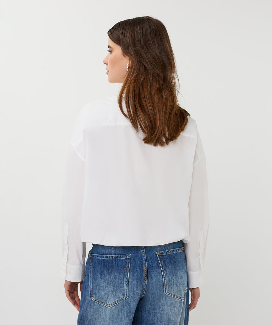 Woman wearing a white blouse and blue jeans against a plain background