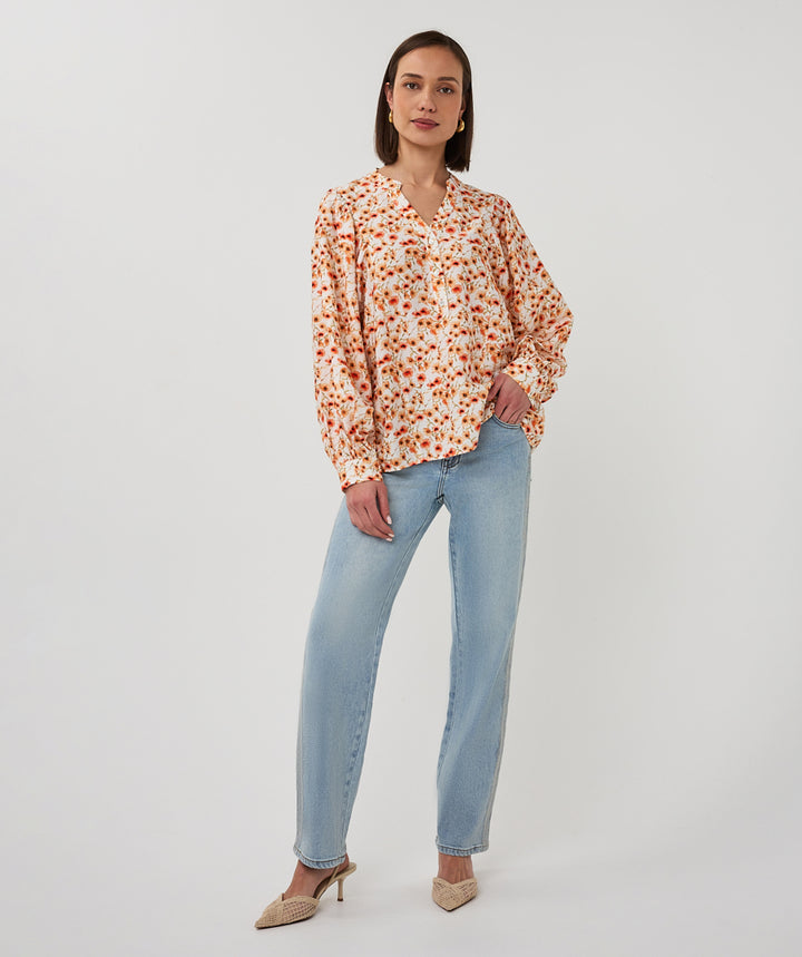 Woman wearing a floral blouse and light blue jeans on a white background