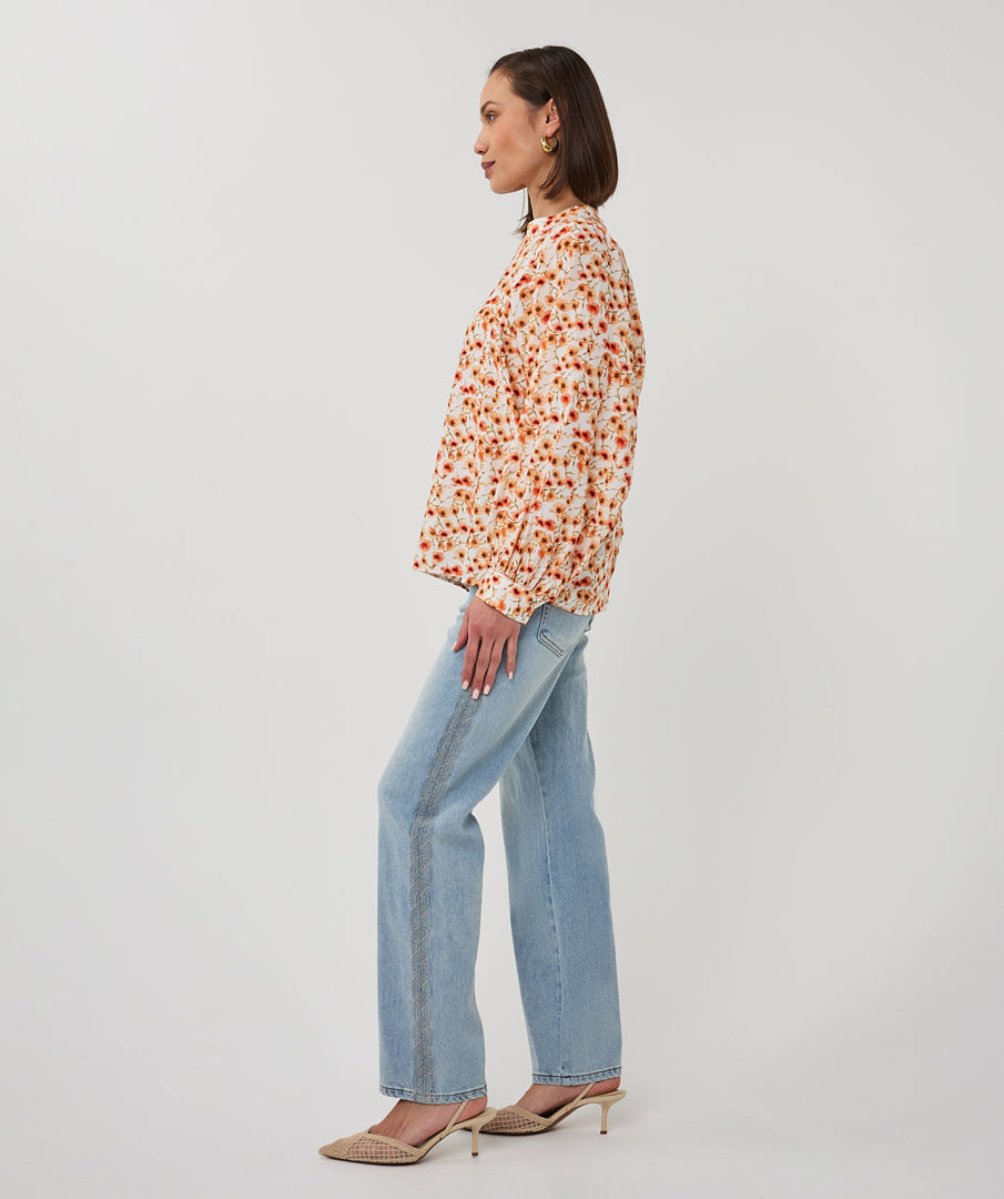 Woman wearing a floral blouse and light blue jeans on a white background