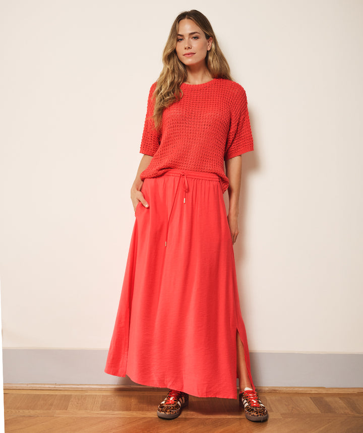 Woman wearing a red outfit standing against a plain wall.