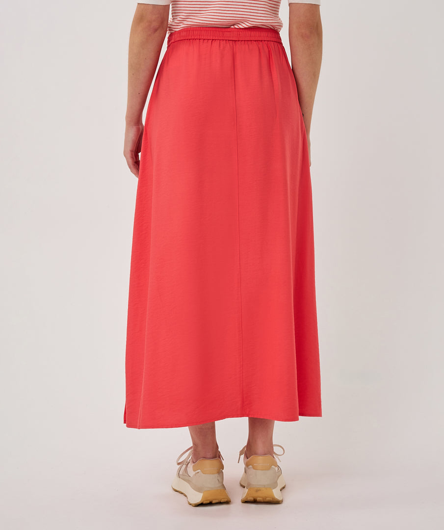 Person wearing a long coral skirt on a plain background