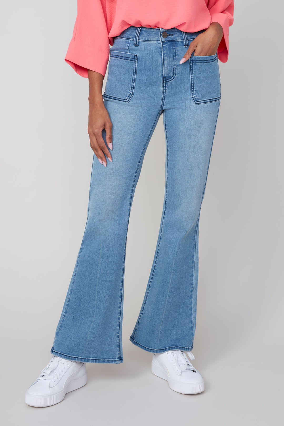 Person wearing blue flared jeans and a pink top on a plain background