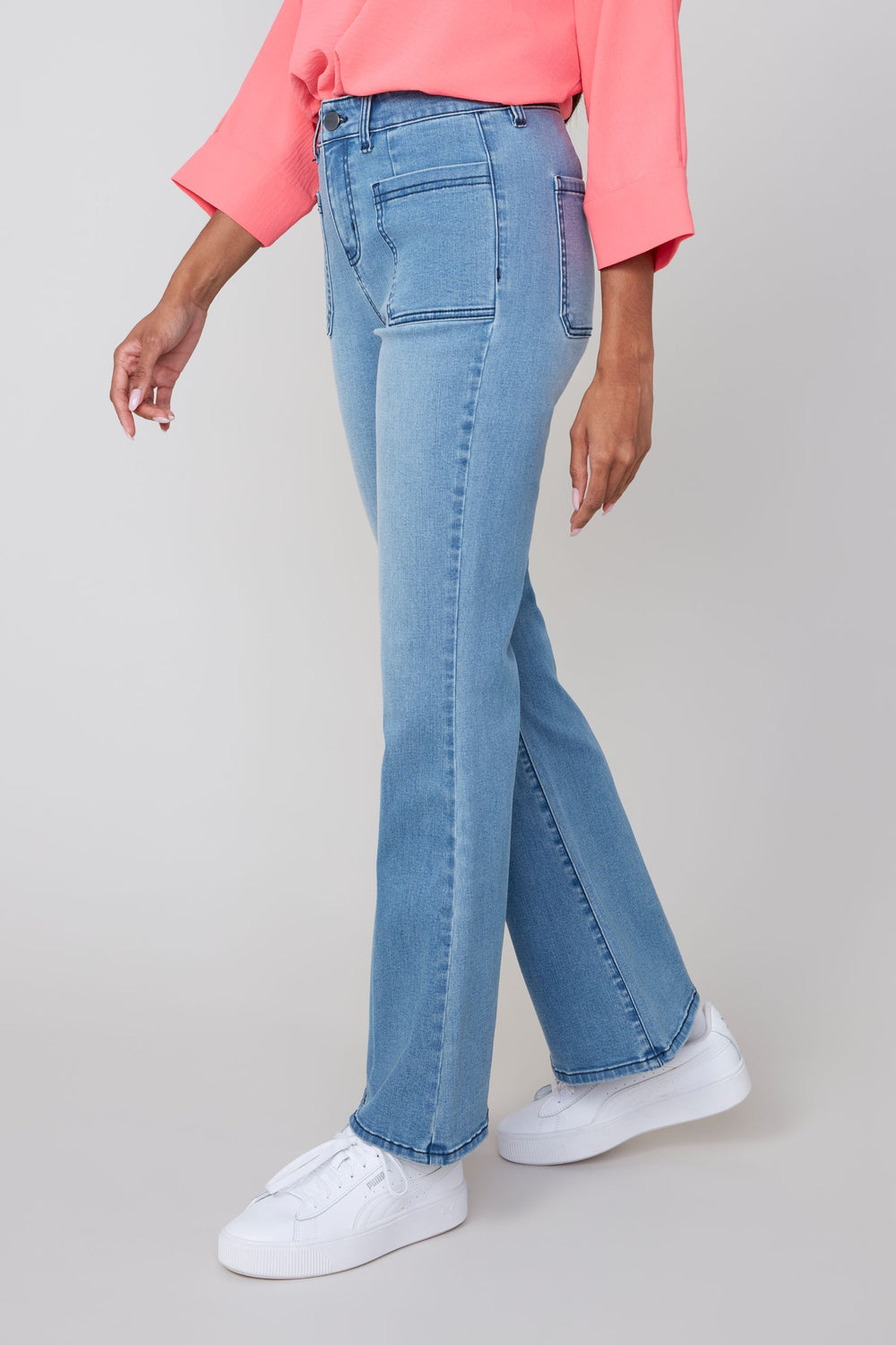 Person wearing light blue flared jeans and a pink top on a gray background