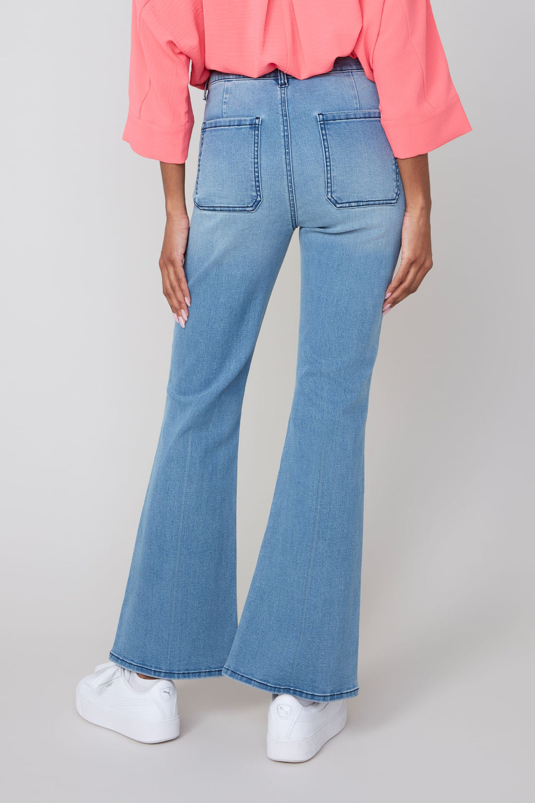 Person wearing light blue flared jeans and a pink top on a plain background