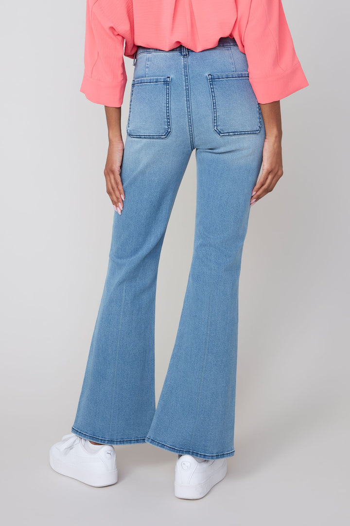 Person wearing light blue flared jeans and a pink top on a plain background