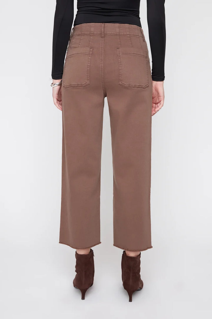 A person shown from the back wearing brown wide-leg cropped pants, a black long-sleeve top, and dark brown ankle boots against a light gray studio background.