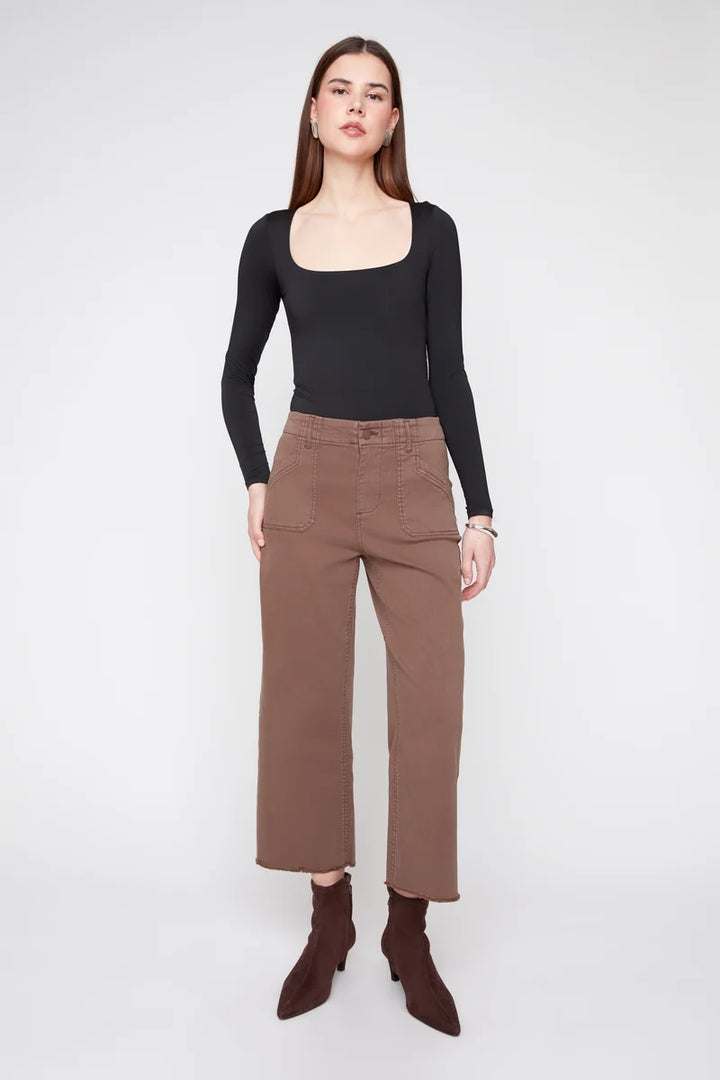 A woman modeling a black long-sleeve top with a square neckline and brown cropped wide-leg pants, paired with dark brown pointed-toe ankle boots, against a light gray studio background.