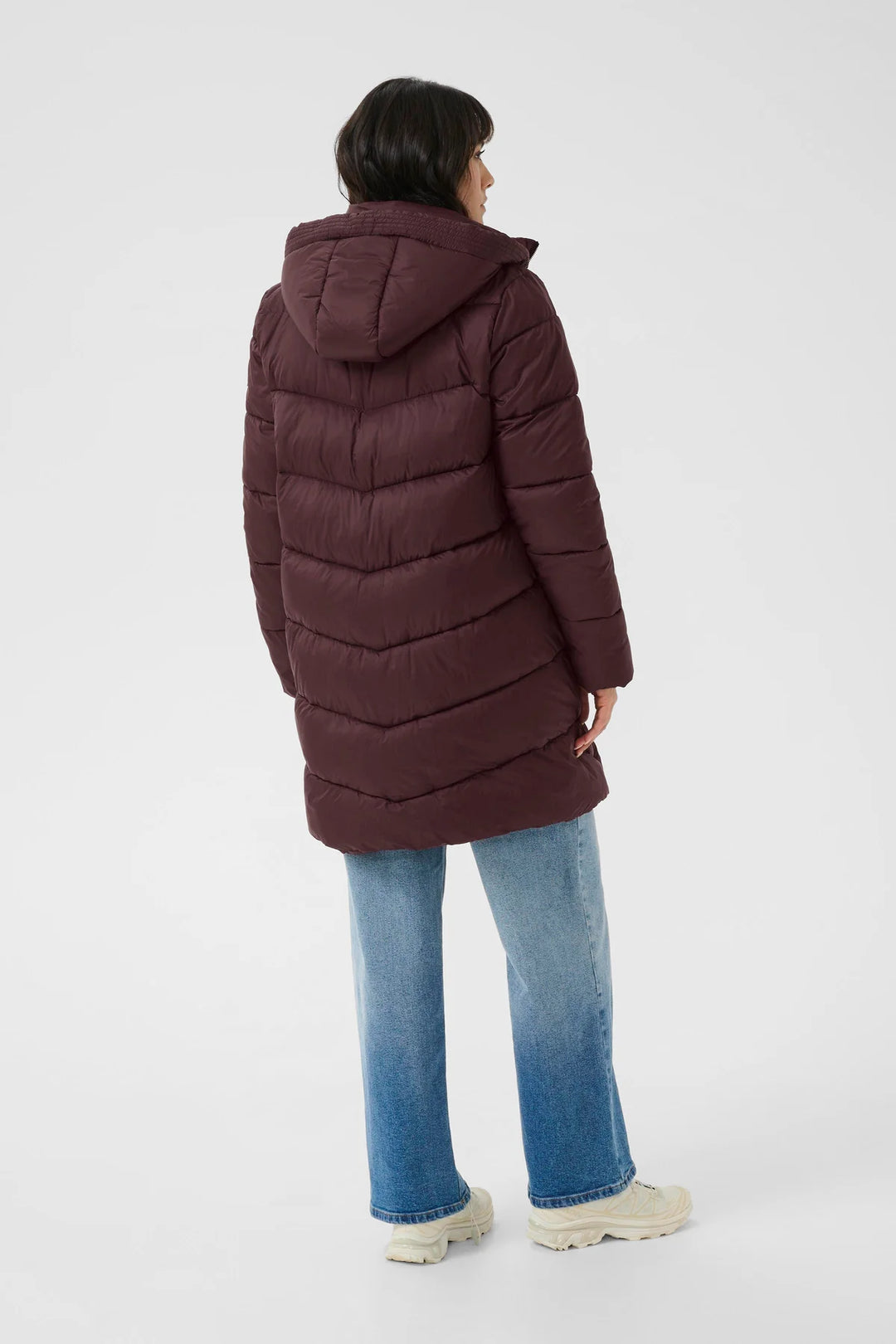 Person wearing a long brown puffer coat on a white background