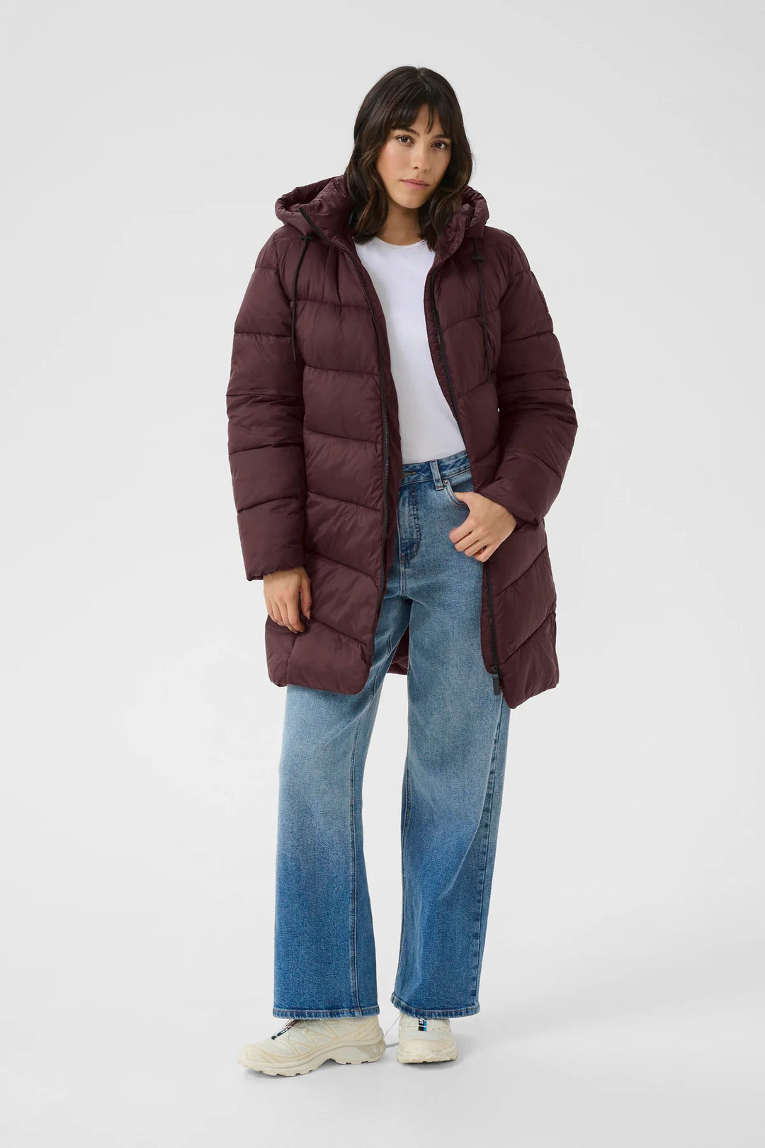 Woman wearing a long burgundy puffer coat on a white background