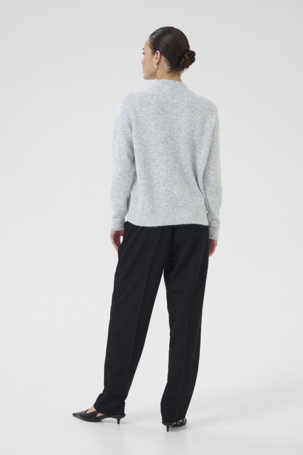 Person wearing a light gray sweater and black pants on a white background