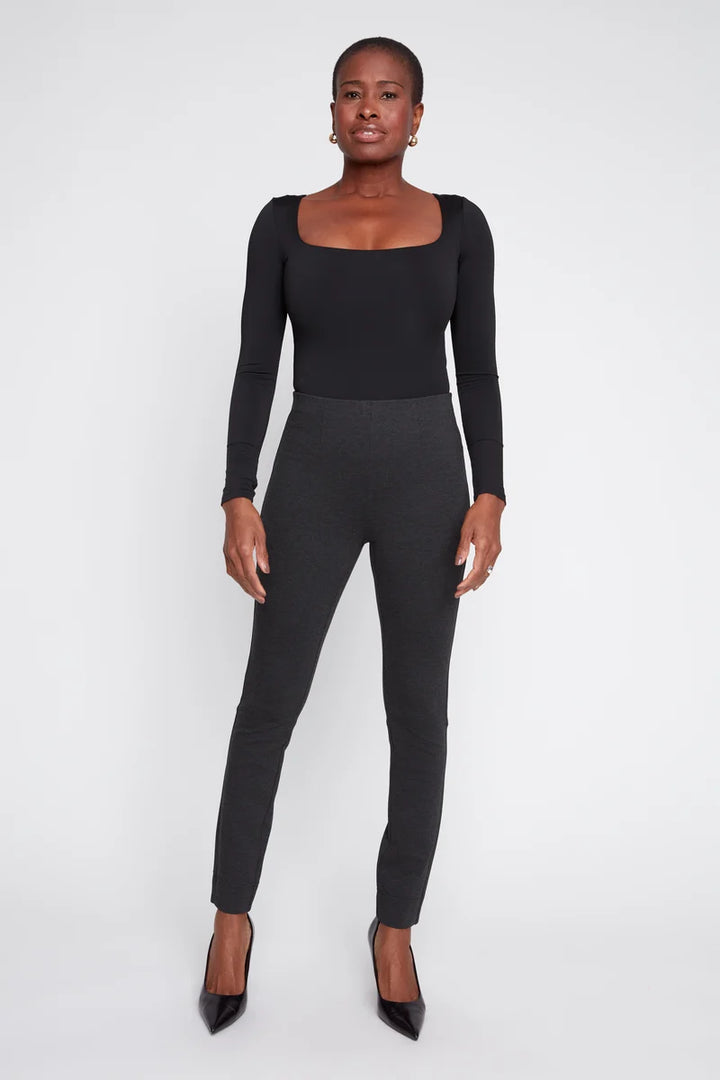 Woman wearing a black long-sleeve top and gray leggings on a white background