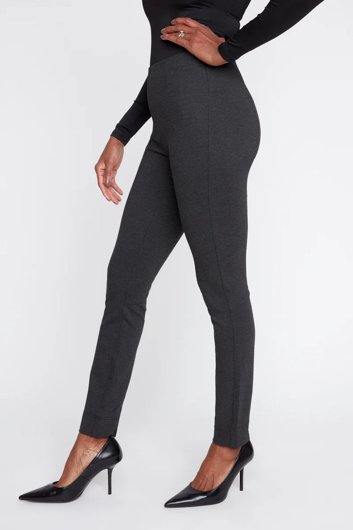 A model wearing dark gray slim-fit trousers with a subtle heathered texture, paired with black pointed-toe stiletto pumps, shown from the waist down against a plain white studio background.