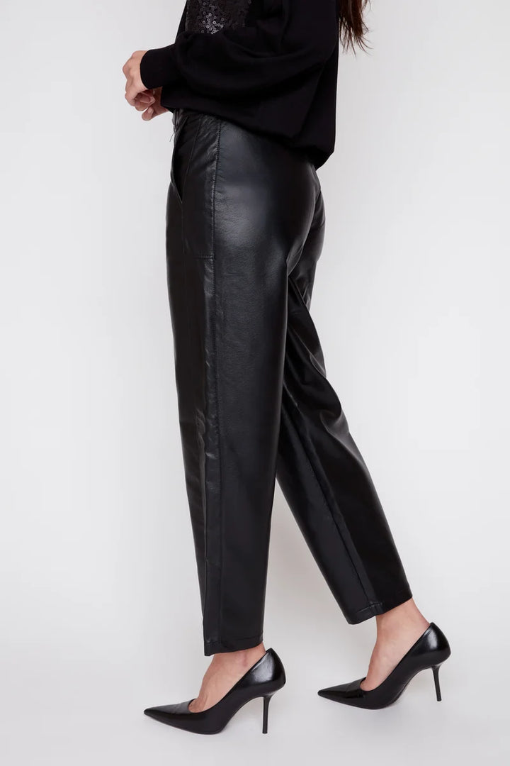 A model wearing black faux-leather cropped trousers, a black top, and black pointed-toe heels, shown from the waist down against a plain white studio background.
