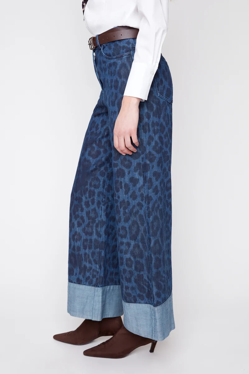 Person wearing blue leopard print pants with a white shirt and brown shoes on a white background