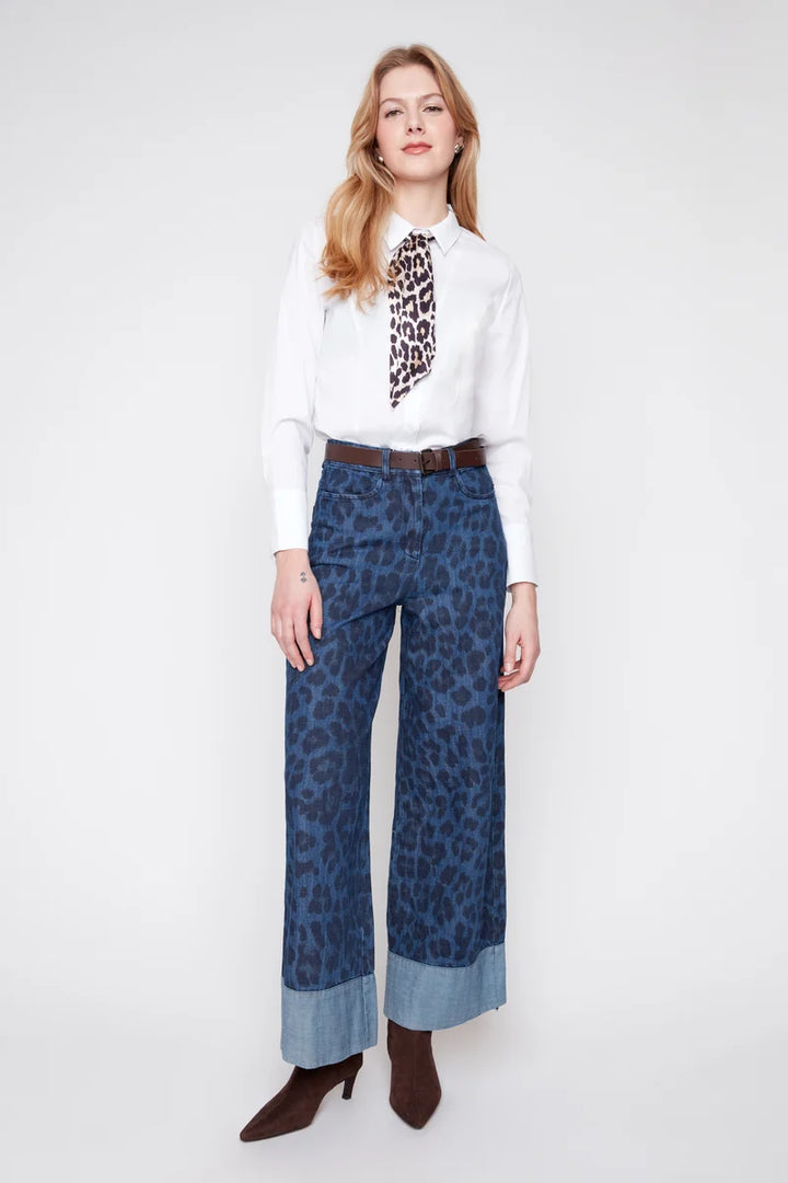 Woman wearing a white blouse with leopard print and blue wide-leg pants on a white background
