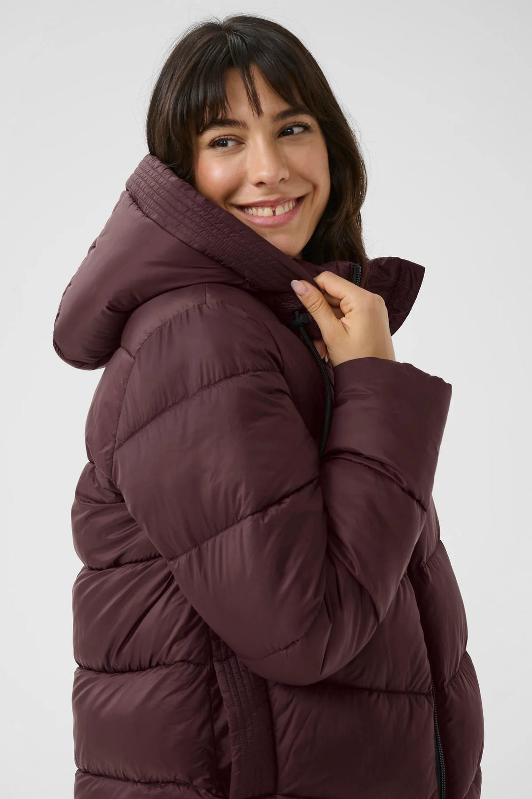 Woman wearing a maroon puffer jacket against a white background