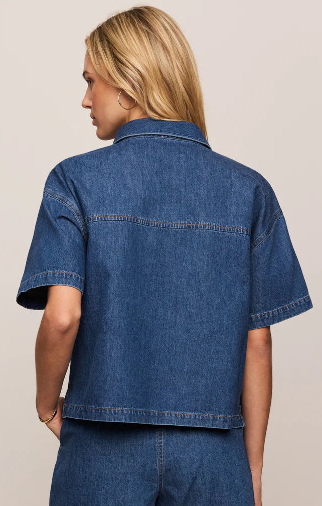 Woman wearing a blue denim shirt and shorts set on a beige background