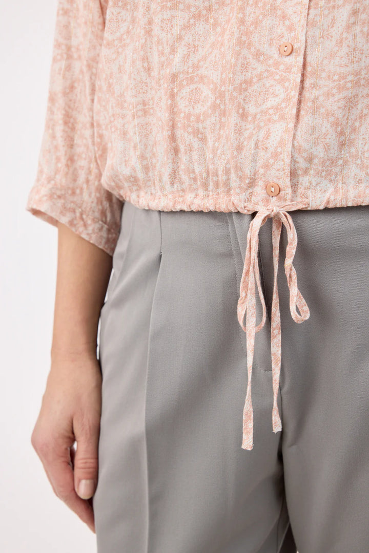 Person wearing a light pink floral blouse and gray pants on a white background