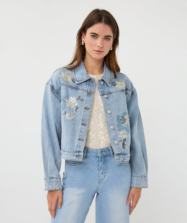 Woman wearing a light blue denim jacket with floral embroidery on a white background