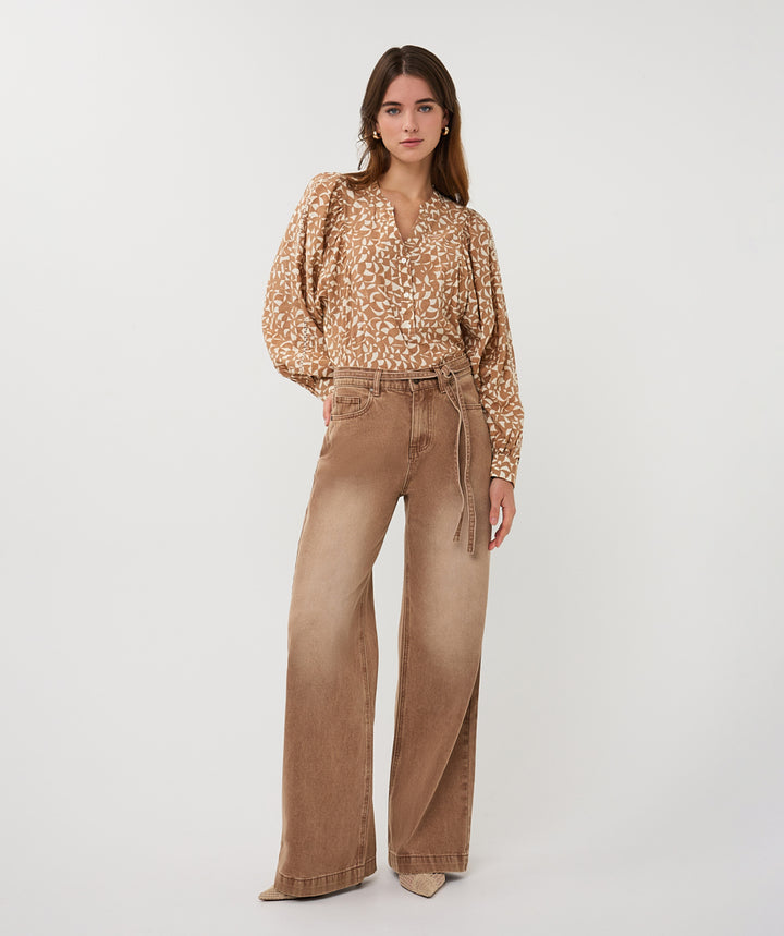 Woman wearing a patterned blouse and brown wide-leg pants on a white background