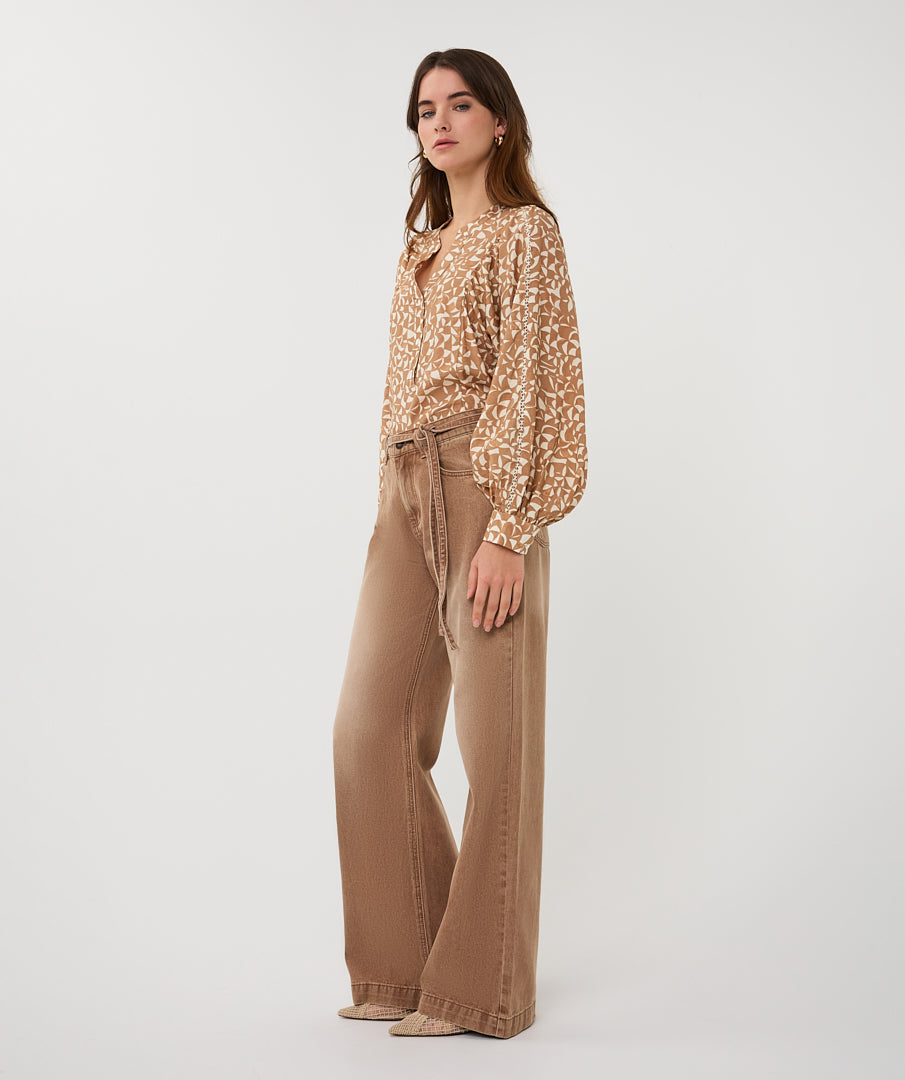Woman wearing a patterned blouse and beige pants on a white background