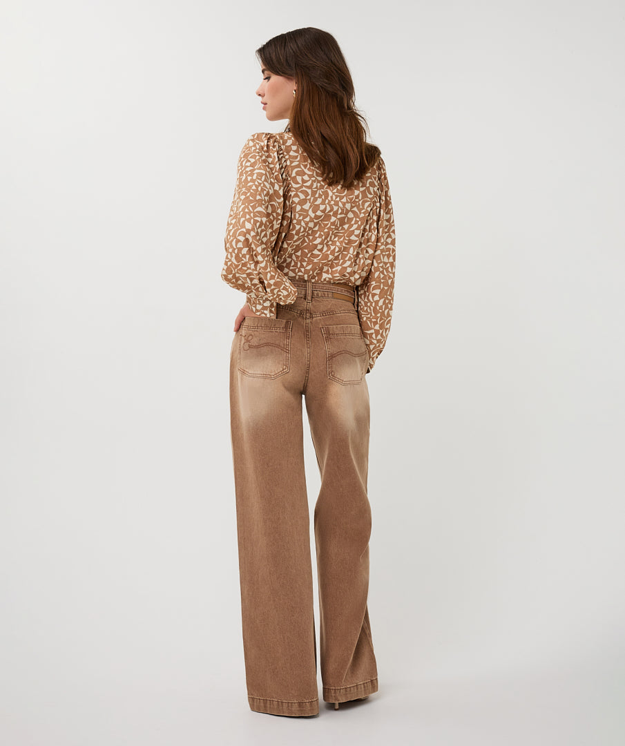 Woman wearing a patterned blouse and tan pants on a white background