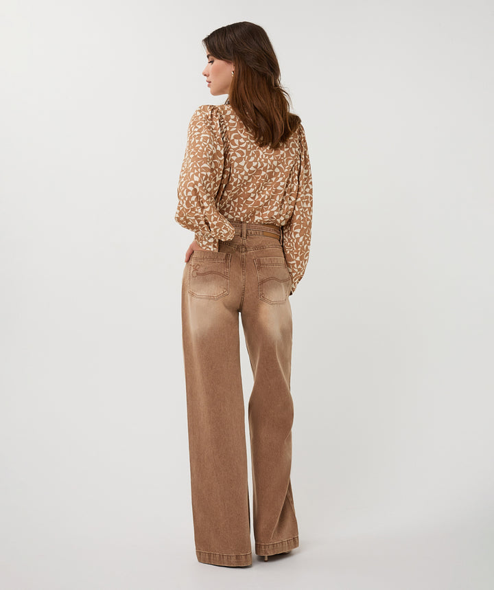 Woman wearing a patterned blouse and tan pants on a white background