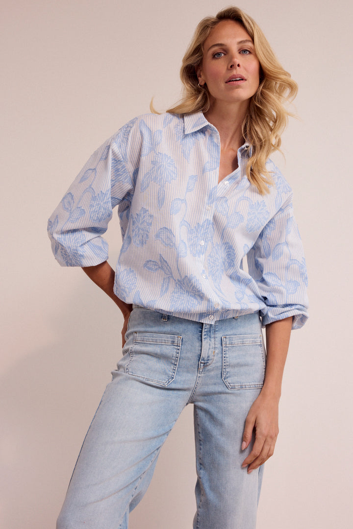 Woman wearing a light blue floral blouse and jeans against a plain background